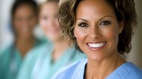 Smiling African American female nurse in blue scrubs with curly hair in hospital setting with diverse medical team colleagues in background.