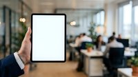 Hand holding tablet with blank screen in modern office environment with blurred colleagues working at desks, suitable for business technology and corporate communication concepts.