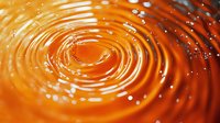Mesmerizing orange liquid ripples with concentric circles and water droplets creating dynamic motion effect on glossy surface. Macro photography of fluid waves.