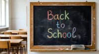 Back to school written in colorful chalk on blackboard in empty classroom with wooden desks and bright window light for education concepts.