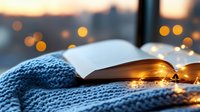 Open book with warm glowing fairy lights on cozy blue knitted blanket against window at sunset, creating atmospheric reading ambiance.