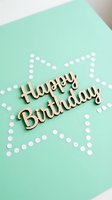 Wooden Happy Birthday lettering on mint green card with white confetti dots forming a star shape, celebrating a special occasion.
