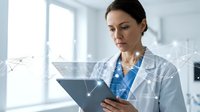 Female doctor in white lab coat using digital tablet with network connections overlay in modern medical office for healthcare technology and telemedicine applications.