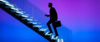 Silhouette of male professional in business suit climbing illuminated staircase against blue and purple gradient background, representing career growth and success.