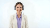 Professional female customer service representative wearing headset and business suit smiling at camera in modern office environment for corporate communications.
