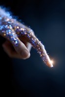 Magical glowing finger covered in sparkling blue and gold glitter dust against dark background, creating ethereal light effect for fantasy and wonder concepts.