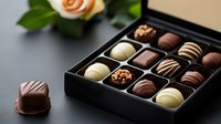 Luxury chocolate pralines and truffles in elegant black gift box with assorted dark, milk and white chocolate bonbons. Single piece placed separately. Rose decoration.