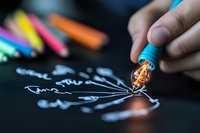 Close up of glowing light bulb tip on creative chalk drawing on black background, artistic concept for ideas and inspiration in education and design.