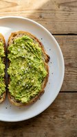 Fresh avocado toast with sea salt and black pepper on rustic sourdough bread served on white plate over weathered wooden table background for healthy breakfast.