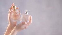 Female hands holding pink perfume bottles against soft pastel background for beauty and fragrance advertising campaigns.
