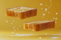 Crispy golden toast slices floating against vibrant yellow background with sprinkles of salt or sugar creating dynamic food composition.