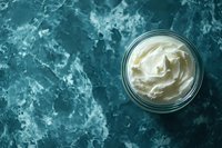 Creamy white whipped butter or cream cheese spread in glass jar on dark turquoise marble background with copy space, top view food photography.