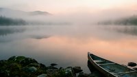 Serene lake at dawn with moored boat, misty mountains, and calm water reflections. Peaceful morning landscape for nature, travel, and meditation projects.
