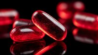 Translucent red capsules with bubbles inside on reflective black surface, dramatic lighting highlighting glossy texture for pharmaceutical or supplement marketing.