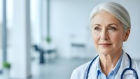 Confident mature female doctor with stethoscope smiling in modern medical office, healthcare professional portrait for medical marketing materials.