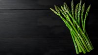Fresh green asparagus spears arranged on dark black wooden background with copy space, top view. Raw organic vegetables for healthy cooking.