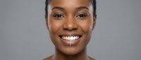 Happy young African American woman with bright smile showing white teeth against gray background for beauty and healthcare concepts.