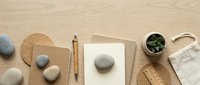 Minimalist workspace with natural stones, wooden pen, notebooks and small plant on beige textured surface for creative projects and mindful planning.