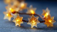 Glowing star-shaped string lights creating magical holiday atmosphere on dark textured background. Warm golden illumination for festive decoration.