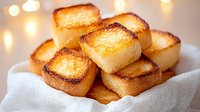 Freshly toasted golden brioche bread cubes with crispy caramelized edges served on white linen napkin against soft bokeh lights background for food photography.