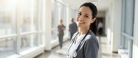 Smiling female doctor with stethoscope in modern hospital corridor. Professional healthcare worker in medical scrubs ready for patient care and consultation.
