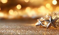 Shiny metallic star decorations on glittering golden surface with warm bokeh lights in background creating festive holiday atmosphere.