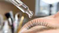 Professional eyelash extension treatment with precision dropper application in modern beauty salon for enhanced lash volume and length.