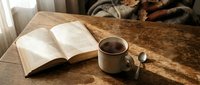 Cozy morning scene with open book and steaming coffee cup on rustic wooden table creating peaceful reading atmosphere for relaxation and leisure time.