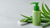 Green cosmetic pump bottle with fresh aloe vera leaves and white stone on light gray background. Natural skincare and beauty product photography.
