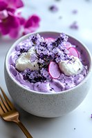 Purple smoothie bowl topped with coconut cream, sliced radish, lavender flowers and black sesame seeds in ceramic bowl with gold fork, food styling.