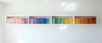 Colorful books arranged by rainbow spectrum on white floating shelf creating organized library display for home office interior design and education.