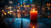 Glowing orange candle on wet wooden surface against blurred city lights and rain drops on window, creating cozy atmospheric evening ambiance.