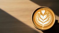 Coffee cup with heart latte art on wooden table with warm sunlight shadows creating cozy cafe atmosphere for morning beverage and relaxation moments.