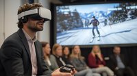 Young Caucasian businessman in VR headset playing virtual skiing game during presentation while audience watches large screen display showing winter sports simulation.