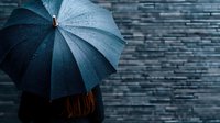 Moody atmospheric composition with teal umbrella against dark brick wall background, water droplets glistening on umbrella surface in dramatic lighting.