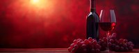 Red wine bottle with filled glass and fresh grapes on wooden table against dramatic red background with sunlight rays creating romantic atmosphere.