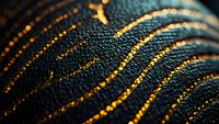 Macro shot of dark denim fabric with glowing golden threads creating curved lines and patterns, showing detailed textile texture and weave structure.