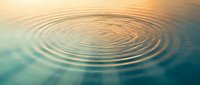 Concentric water ripples spreading across calm surface with golden sunset reflection creating peaceful zen-like atmosphere for meditation and wellness concepts.