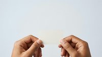 Hands holding blank white card or paper against neutral background for mockup, branding, advertising, or presentation purposes.