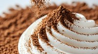Creamy white whipped topping swirled in spiral pattern with cocoa powder sprinkled on top, extreme close up macro shot showing texture and detail.
