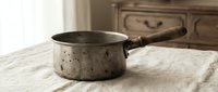Vintage speckled enamel saucepan with wooden handle on marble countertop in rustic kitchen setting for cooking and food preparation concepts.