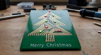 Electronic circuit board Christmas tree design on green PCB with gold traces and red components creating festive holiday greeting card for tech enthusiasts.
