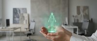 Futuristic holographic human figure projection floating above open palm in modern office workspace showcasing advanced technology and digital innovation concepts.