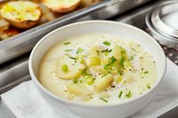 Creamy potato soup garnished with fresh chives and black pepper in white bowl, comfort food served hot with tender potato chunks and aromatic herbs.