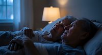 Senior couple sleeping peacefully together in bed at night with warm lamp light creating intimate bedroom atmosphere for health and relationship concepts.