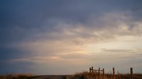Dramatic sunset sky with wooden fence posts silhouetted against colorful twilight clouds over rural countryside landscape for nature and agricultural themes.