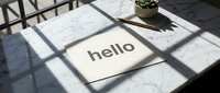 Card with hello text on marble table in sunlight with shadows, gold pen and succulent plant, minimalist greeting concept.