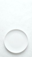 Empty white ceramic plate on textured white surface, overhead view. Suitable for food styling, restaurant menus, culinary blogs, and dining concepts.