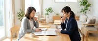 Two professional Asian businesswomen having meeting at wooden table in bright modern office discussing documents and paperwork for corporate consultation.