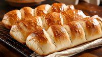 Freshly baked soft dinner rolls with golden brown tops arranged in rows on parchment paper, showing fluffy texture and buttery glaze. Perfect for family meals.